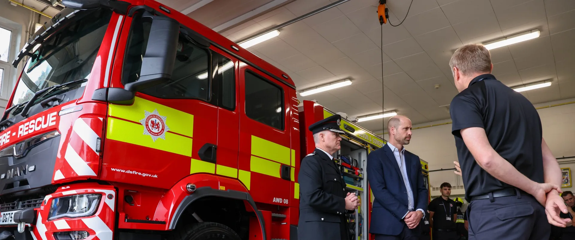 HRH, Prince William, The Prince of Wales, with a fire officer beside a fire engine, talking to firefighters at their station.