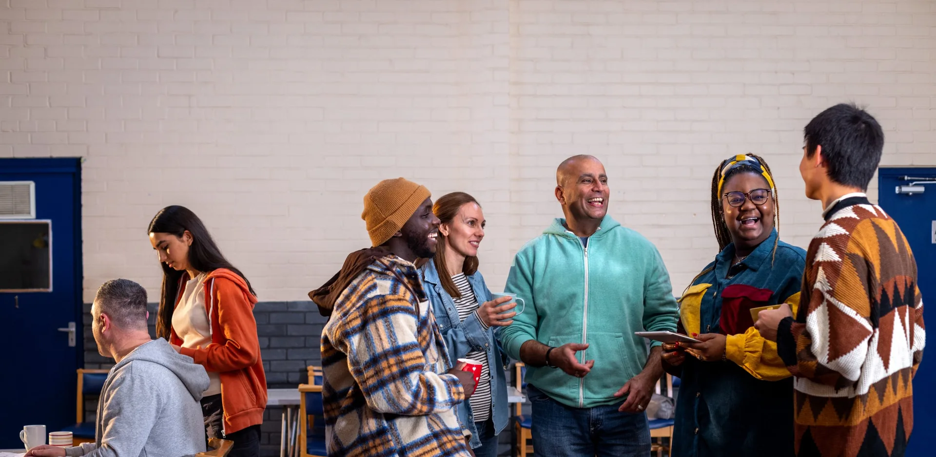 A group of people laughing together over cups of tea in a community hall.