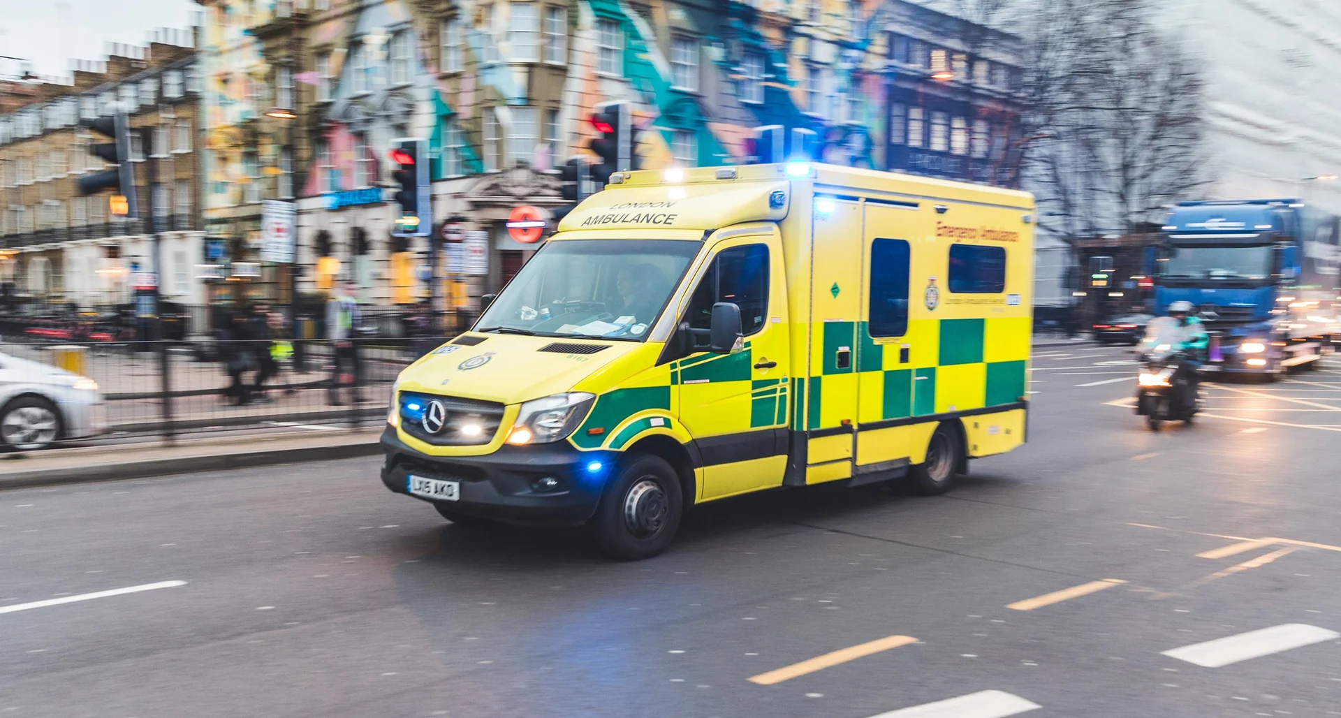 An ambulance with its blue lights on, driving through a London street.