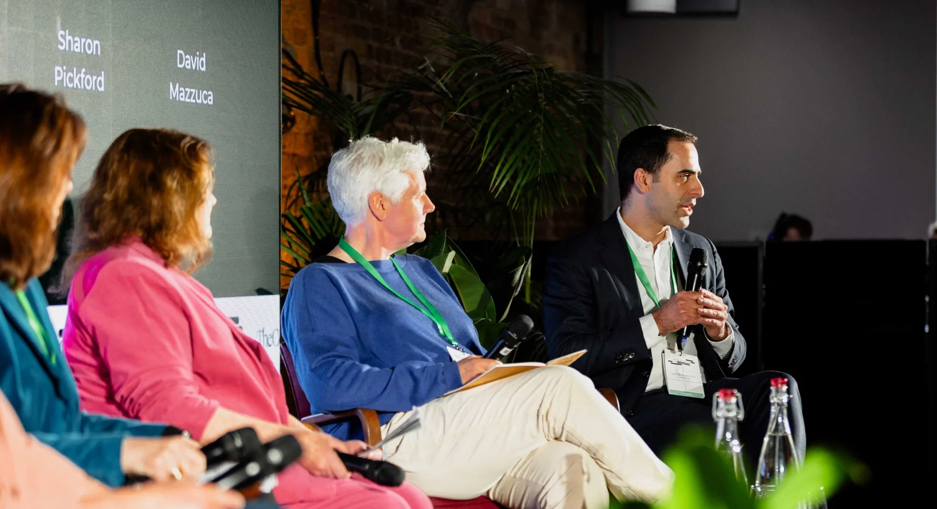 Panel speakers seated on stage at an event, one of them speaking into a microphone.