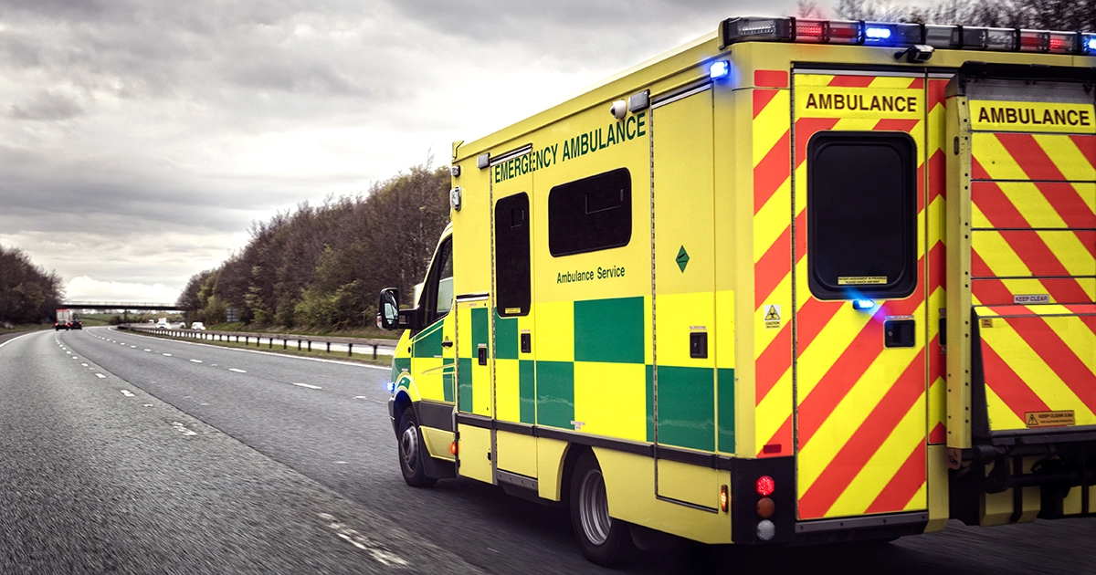 An emergency ambulance with blue lights on, driving along a motorway.