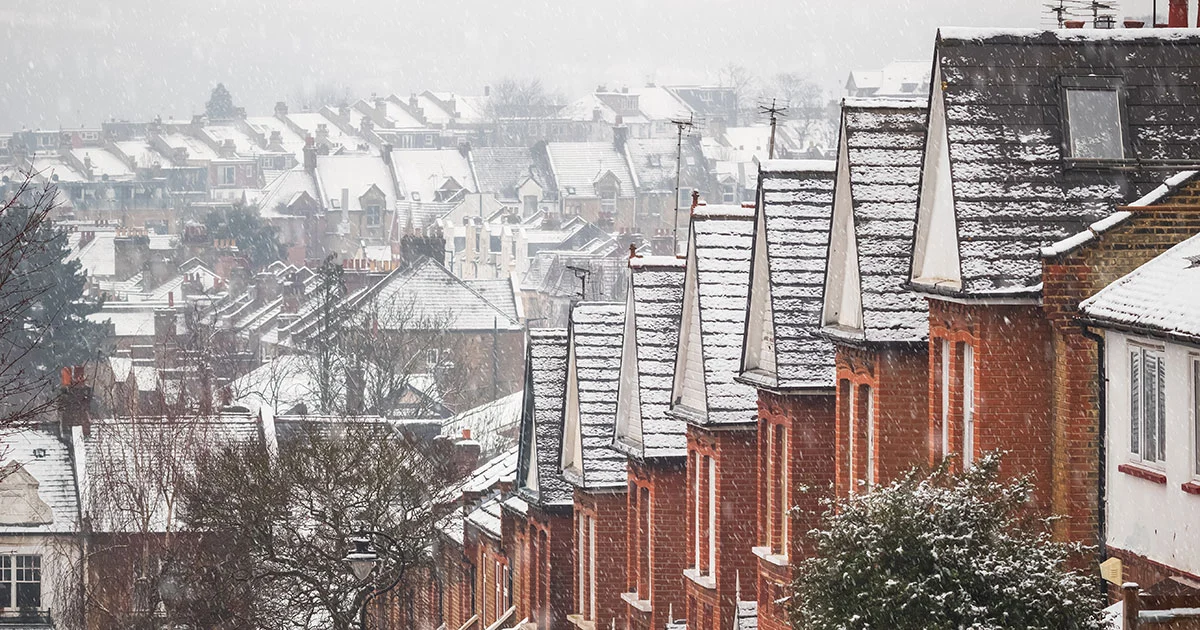 Snow on the roofs of a long row of terraced houses on a hillside.